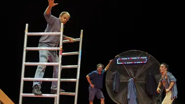 A man balances on two pieces of scaffolding as two others watch on.