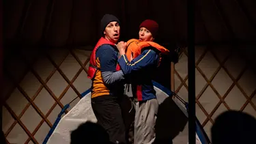 Two performers wearing life jackets hold onto each other with concerned looks.