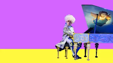 A man wearing a Mozart costume and a big white wig sitting at a grand piano