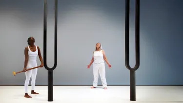 Two artists dressed in white stand below two large tuning forks.