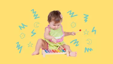 A baby sitting on the floor playing a coloured toy xylophone.