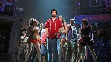 A group of people in colorful clothes, standing and singing on stage.