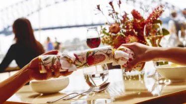 Two hands grab two sides of a christmas cracker with the harbour bridge in the background.