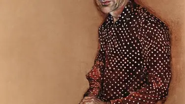 A man in with grey hair in a spotted shirt against a brown background.