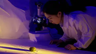 A woman in a white shirt leans over a white floor which has a small round object on it.