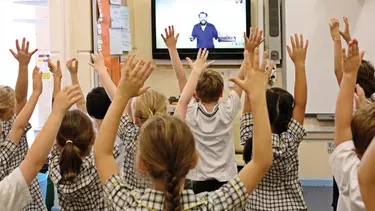 Kids in a digital classroom with their hands up in the air.