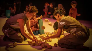 Artists and children explore building blocks on the floor.