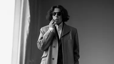 A mature white woman smoking a cigarette. The image is in black and white and she is wearing sunglasses.