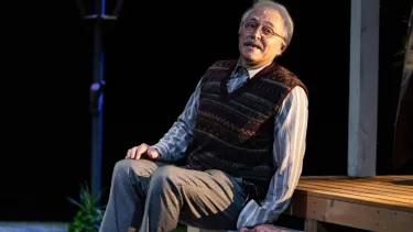 A man wearing glasses sits on a porch step. He is leaning across as if in conversation with someone.