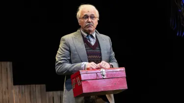 A man in a grey suit holds up a red toolbox.