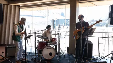 A band on a small stage in front of glass windows.