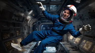 Lano floating in fake spaceship in  his blue astronaut suits, looking concerned heading into space