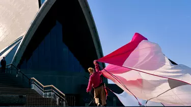A woman outside Sydney opera house holding a long curtain.