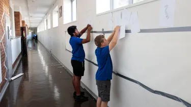 Children putting up posters in a hallway at school.