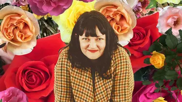 A women smiling infront of a background of flowers