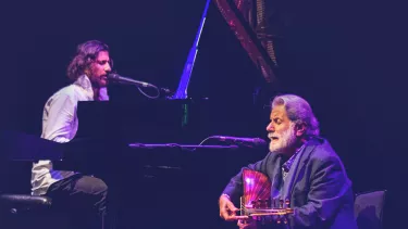 Two men playing grand piano and a guitar.