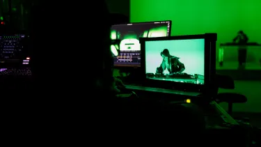 Producer's view through screens of a person standing over a deck in a recording room under a green light