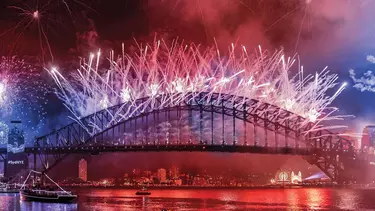 The Sydney Harbour Bridge at night with red and blue fireworks overhead.