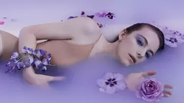 An opera Adriana Lecouvreur laying in purple pool of water with flowers around her.