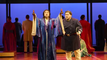 A woman holds two stones aloft while a man in a blue military suit sings behind her.