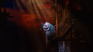 An Asian woman and white man embrace and kiss on stairs.