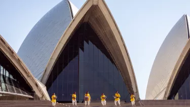 A group of people in yellow and white, playing instruments on the stairs outside the Sydney Opera House.