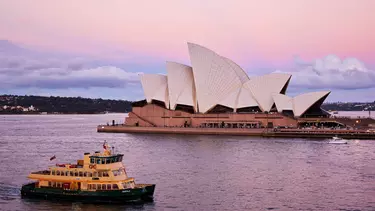 A ferry passing in front of the Sydney Opera House under a pink sky.