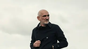 A man with grey hair in a black coat standing outside.