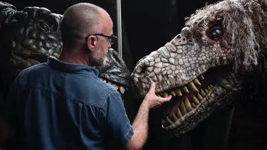 A man stands in front of two dinosaur puppets.