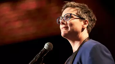 A woman with short hair and glasses standing in front of a microphone, looking into the distance.