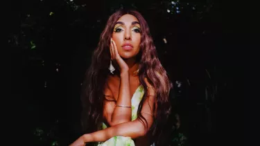 Rupi Kaur a Canadian poet sitting on a chair in a green dress.