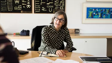 A woman with grey hairs sitting on a chair in an office.