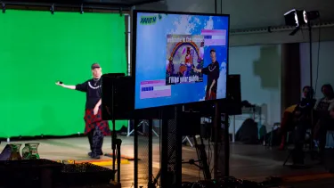Producer's view through a screen showing a digital background, of a performer in front of a green screen