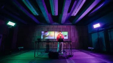 A person standing in a dark room with two screens in the background