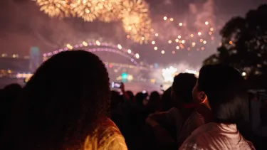Point of view two people watching yellow fireworks over the Sydney Harbour Bridge.