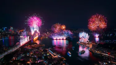 Bird’s eye view of Sydney Harbour and multicoloured fireworks over the Sydney Harbour Bridge and the Sydney Opera House.