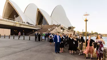 A group of people in wedding attire standing outside of the Sydney Opera House.