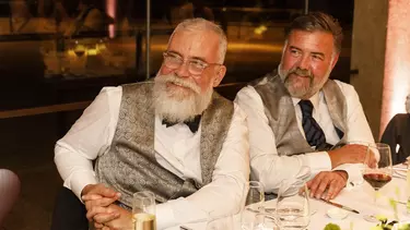 Two men sat at a table, smiling in silver waistcoats.