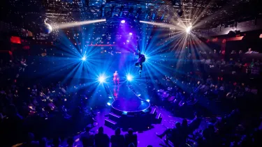 An acrobat is suspended in the air surrounded by a seated crowd.