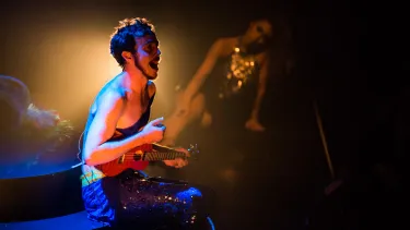 A man sits on stage strumming a ukulele.