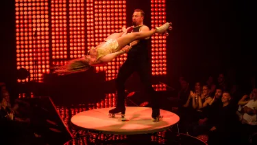 A man in roller skates swings a woman in roller skates on stage