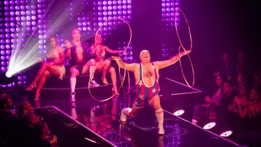 A cheerful man swings four hula hoops around is arms as 3 back up dancers look on.
