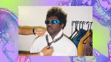 An Indigenous man in sunglasses is casually helped with a tie. The background is a purple, iridescent swirl, looking like water.