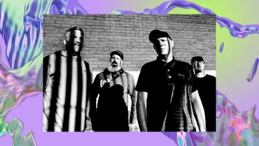 Four men stand against a brick wall in black and white.