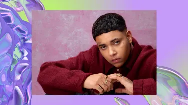 A woman with short dark hair and a tattoo above one eyebrow, wears a burgundy sweater. The background is an iridescent purple swirl, looking like water.