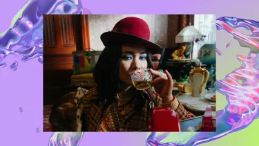 A woman in a red hat and plaid coat with bright blue eyeshadow drinks from a glass, surrounded by eclectic, vintage decor and a retro telephone. The background is an iridescent, purple swirl, looking like water.