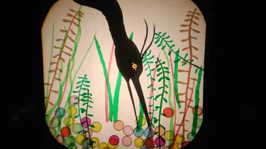 A bird is reaching its beak through plants to pick up coloured circles.