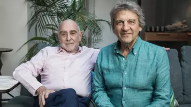 Two men sat together, one in a green shirt and one in a pink shirt.