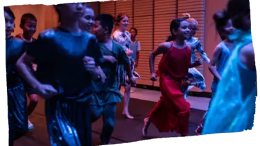 A group of children are running along a black floor with a wooden wall behind them.