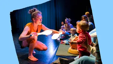 A woman holds two glowing juggling pins while a child sits on the floor, both engaged in a playful moment together.